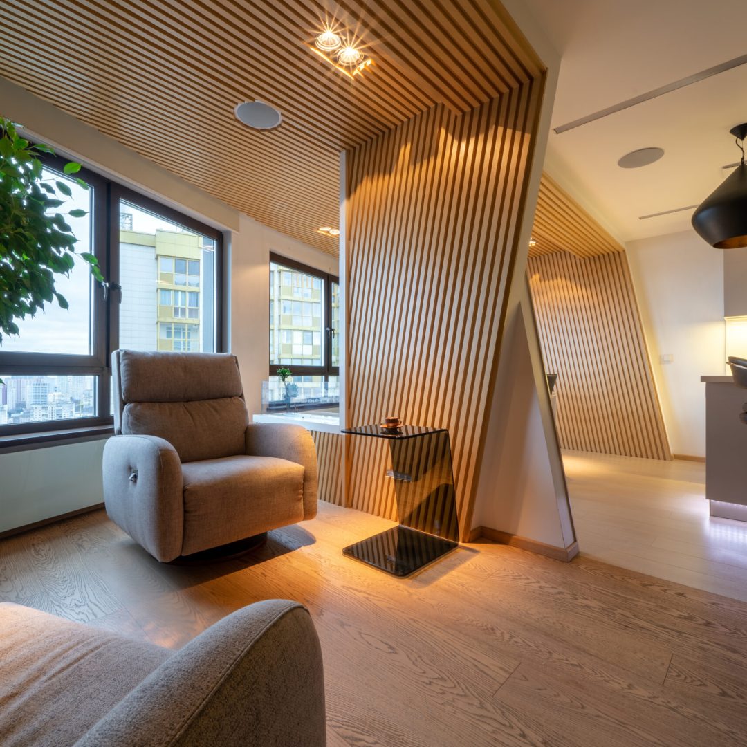 Luxury studio apartments in wooden colors with soft armchairs. Stylish modern kitchen area with bar counter and modern lamps